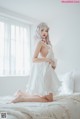 A woman in a white dress sitting on a bed.