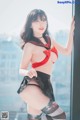 A woman in a red and black lingerie posing by a window.