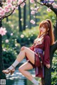 A woman in traditional attire poses by a tree with cherry blossoms.