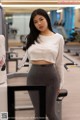 A woman in a white top and gray leggings posing in a gym.