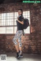 A woman standing in front of a brick wall holding a backpack.