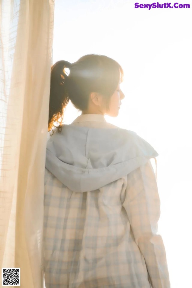 A woman standing in front of a window looking out the window.