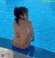 A woman in a bikini sitting on the edge of a swimming pool.