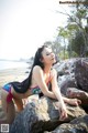 A woman in a bikini sitting on a rock on the beach.