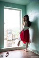 A woman in a red dress standing by a window.