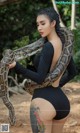 a woman in a black bodysuit holding a large snake