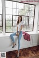 A woman sitting on a window sill in a white shirt and jeans.