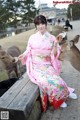 A woman in a pink kimono sitting on a bench next to two deer.