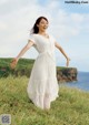 A woman in a white dress standing on a grassy hill.