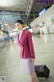 A woman in a pink jacket and skirt holding a black suitcase.