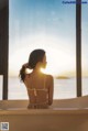 A woman in a white bikini sitting in a bathtub looking out a window.