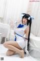 A woman in a white and blue dress sitting on a bed.