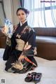 A woman in a kimono sitting on a bed holding a fan.