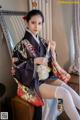 A woman in a kimono sitting on a chair holding a fan.