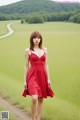 A woman in a red dress standing on a dirt road.