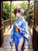 A woman in a blue kimono standing on a wooden walkway.