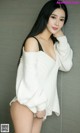 A woman in a white sweater leaning against a wall.