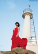 A woman in a red dress standing on a rock near a lighthouse.