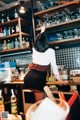 A woman standing behind a bar with a lot of bottles on the shelves.