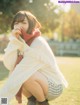 A woman in a white sweater and a red scarf sitting on the grass.