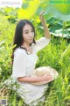 A woman in a white dress and straw hat sitting in the grass.